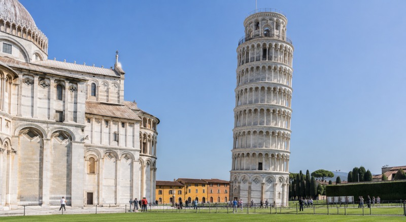 Imagem realista da Torre de Pisa, na Itália, destacando sua famosa inclinação em meio à arquitetura histórica e aos jardins da Piazza dei Miracoli, sob iluminação natural